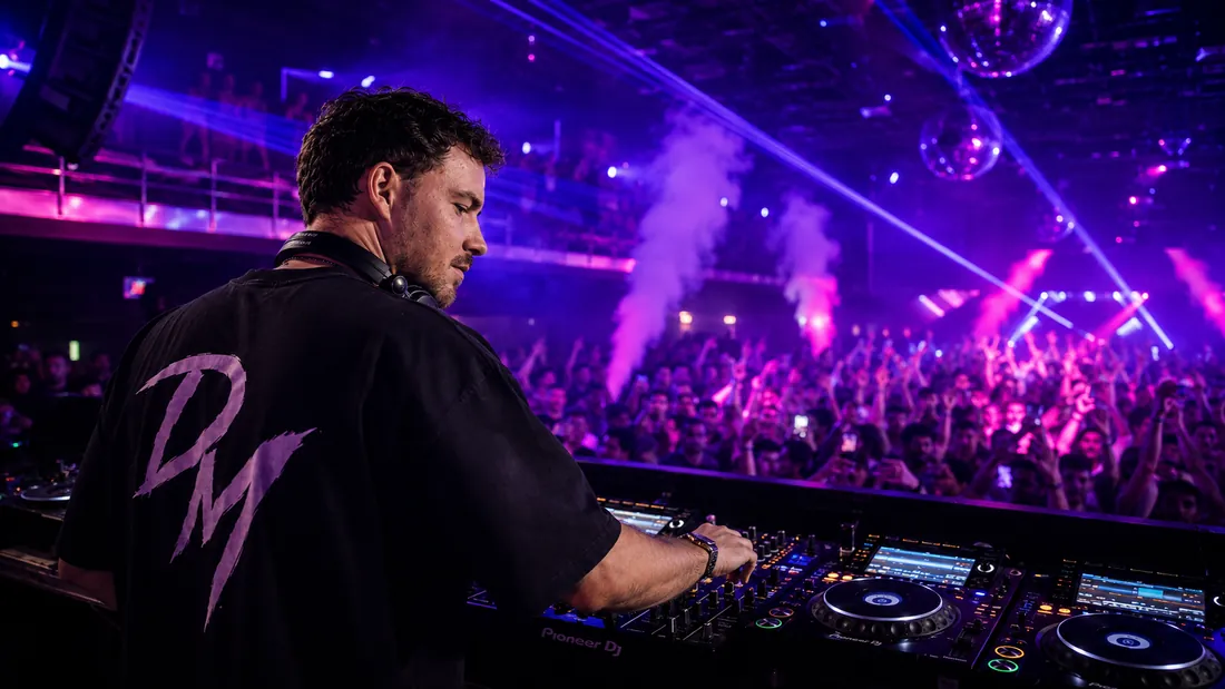 Dennis Masur im Profil am Pult, konzentriert auf den Mixer, im Hintergrund violette Scheinwerfer